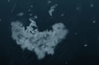 Image of a blob of white fluffy-looking material in the center with other bits around it, on a dark blue watery background.