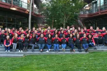 Group photo showing dozens of Stanford Bio-X graduate students seated on steps at the Clark Center, wearing matching shirts and with their arms around each other.