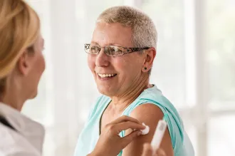 Photo of a female doctor having given an older woman an injection in the upper arm, holding a cotton ball to the site.