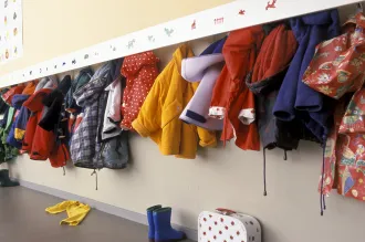 Photo of colorful children’s coats hung up on a wall rack.