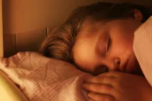 Photo of little girl sleeping in a bed with her hand beside her pillow.