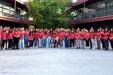Outdoor photo of 70 Stanford undergraduate students wearing matching pale red T-shirts with the Stanford Bio-X logo and smiling at the camera, all standing in the Clark Center Courtyard.