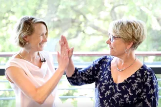 Photo of two female faculty members high-fiving in front of a window.