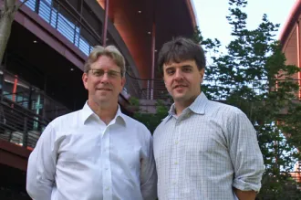 Outdoor photo of two male faculty members standing together and smiling.