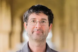 Photo of a white male faculty member in glasses standing in one of Stanford's arcades.