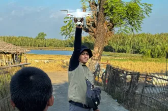 A local drone pilot, Muh. Yusuf Fadhel Marwiji, in Makassar, Indonesia, prepares to launch a drone to search for discarded tires that collect rainwater and become mosquito breeding sites, as a curious child watches