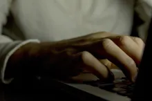 Photo of a man using a computer in the dark, showing only his hand on the keyboard and not his face.