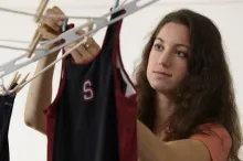 Photo of undergraduate girl hanging Stanford-logo running tops on a rack with clothespins.