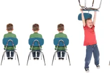 Photo of line of children sitting in chairs, with one child acting out.