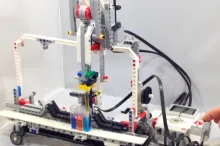 Screnshot from video showing researcher controlling Lego robot with a few button pushes, and robot pipetting liquids in different tubes.