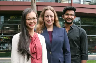 Outdoor photo of a young Asian female medical student, a white female faculty member, and a young southeast Asian male undergraduate student smiling at the camera together.