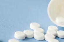 Photo of white bottle spilling white pills across a blue surface.