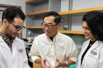 Indoor photo of Stephan Ramos, Professor Seung Kim, and Preksha Bhagchandani in the lab.