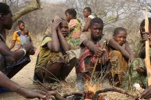 Photo of several members of the Hazda hunter-gatherer tribe in Tanzania crouched around a fire.