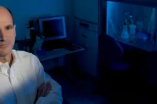 Photo of Dr. Thomas Rando in the laboratory, with fume hood lit up blue in the background.