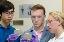 Photo of students Christian Choe, left, Zach Rosenthal and Maria Filsinger Interrante, examining petri dishes in the laboratory.