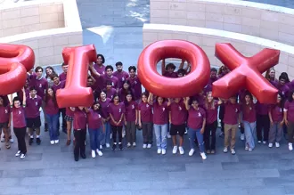 Outdoor photo of 76 students wearing matching red shirts and holding up inflated letters reading "Bio X"