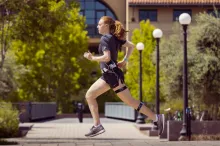 Photo of white female graduate student running across a courtyard area at Stanford, wearing running clothes and the wearable device described in the article.
