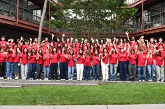 Outdoor photo of 86 undergraduates in matching shirts, waving.