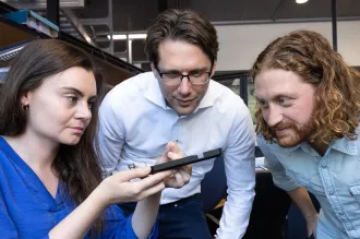 Photo of faculty member and two researchers looking at a device in the lab.