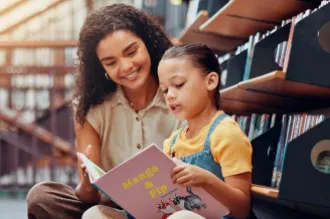 Photo of a child reading from a picture book with a woman looking over her shoulder.
