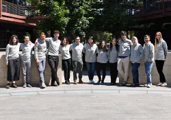 Outdoor photo of 13 postdocs in matching Bio-X sweaters in the Courtyard.