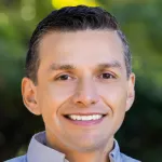 Photo of a smiling Latino man with short dark hair, Dr. Andres Carenas, Assistant Professor of Epidemiology and Population Health at Stanford University.