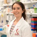 Photo of a female graduate student standing in a wet laboratory, wearing a lab coat with the Bio-X logo and smiling at the camera.
