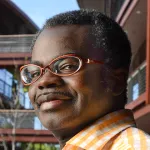 Photo of a smiling Black male faculty member wearing glasses, Dr. Kwabena Boahen, Professor of Bioengineering and Electrical Engineering at Stanford University.