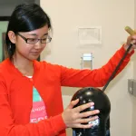 Photo of a female graduate student adjusting a test dummy head using a metal rod in a laboratory.