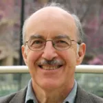Photo of while male professor wearing glasses and smiling, with a gray mustache.
