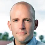 Photo of a smiling white male faculty member with a shaved head, standing outdoors, Dr. Steve Collins, Associate Professor of Mechanical Engineering at Stanford University.