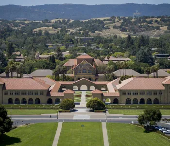 Outdoor overhead photo of Stanford campus, focused on the entrance to the main quad with the Memorial Church facade visible, with the foothills in the background.