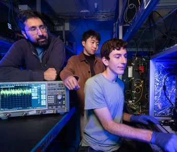Interior laboratory photo of Stanford doctoral student Devin Dean preparing to measure an optical amplifier chip with Amir Safavi-Naeini and Taewon Park watching over his shoulder.