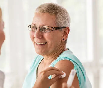 Photo of a female doctor having given an older woman an injection in the upper arm, holding a cotton ball to the site.
