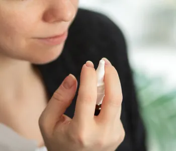 Photo of a woman raising a nasal spray in her hand.