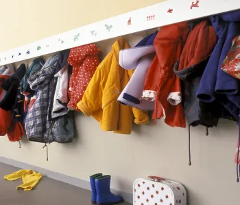 Photo of colorful children’s coats hung up on a wall rack.