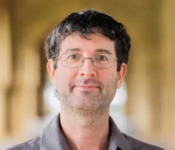 Photo of a white male faculty member in glasses standing in one of Stanford's arcades.