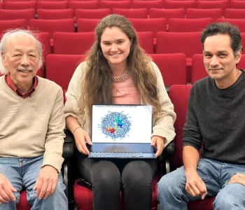 Photo of Professor Wah Chiu, graduate student Rachael Kretsch holding a laptop showing a colorful structure on the screen, and Professor Rhiju Das, all seated indoors and smiling at the camera.