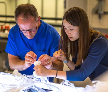 Photo of a male and female scientist both leaned over a plastic device on an illuminated table, adding wires to it.