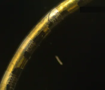 Image of a thin gold plated wire arcing across a black background.