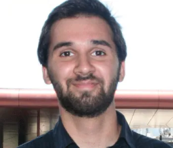 Photo of male faculty member and female postdoc standing in the lab, wearing white lab coats and smiling, with a computer screen showing cell images.