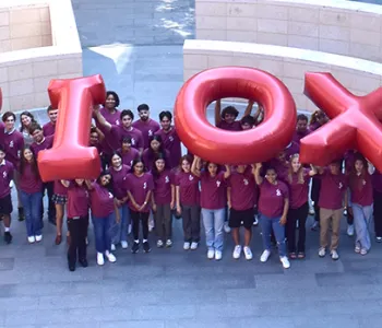 Outdoor photo of 76 students wearing matching red shirts and holding up inflated letters reading "Bio X"