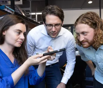 Photo of faculty member and two researchers looking at a device in the lab.