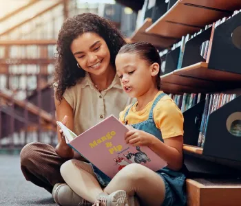 Photo of a child reading from a picture book with a woman looking over her shoulder.