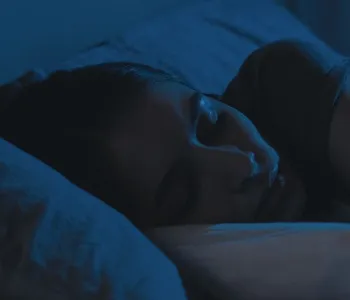 Dark blue tinted photo of a woman's head resting on a pillow as she sleeps.