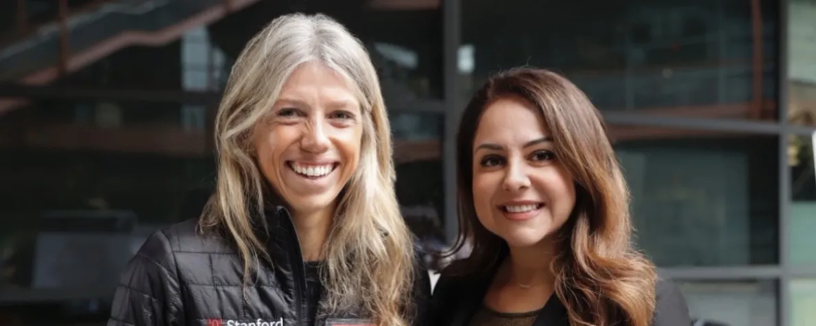 Photo of two women standing together outdoors, smiling at the camera.