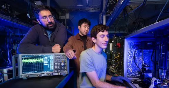 Interior laboratory photo of Stanford doctoral student Devin Dean preparing to measure an optical amplifier chip with Amir Safavi-Naeini and Taewon Park watching over his shoulder.