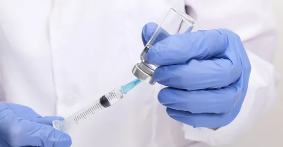 Photo of a scientist's gloved hands holding a syringe with a cap.