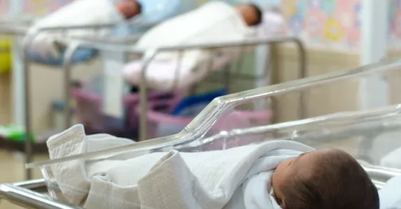 Photo showing newborn baby in hospital crib in foreground, with two more babies in the background.